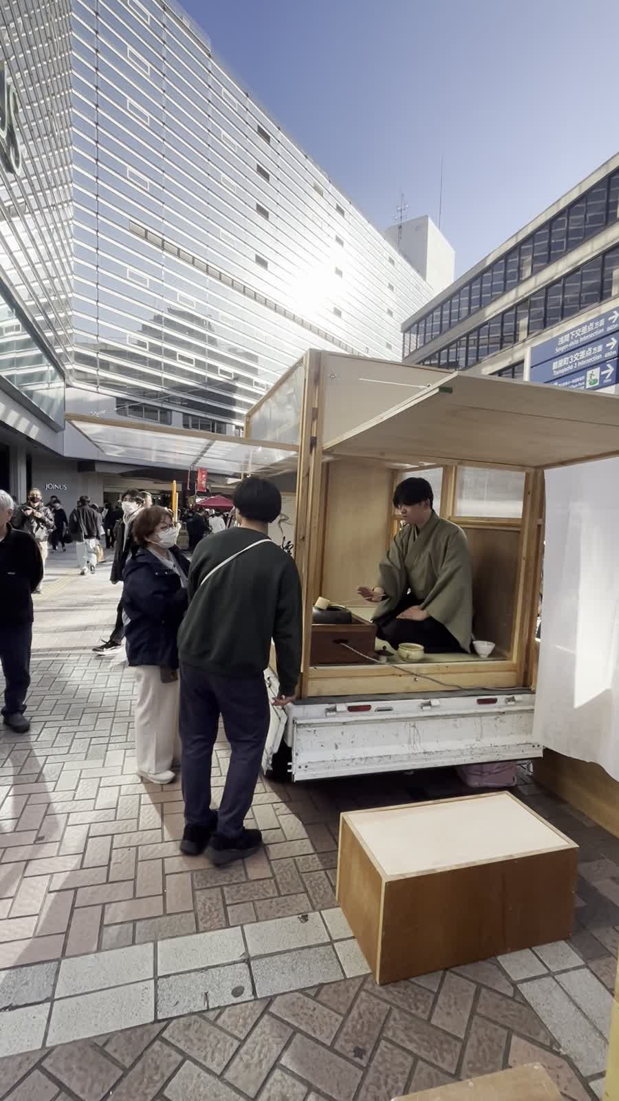 横浜の歩行空間に停めた軽トラ茶室で、亭主がお茶を点てる様子